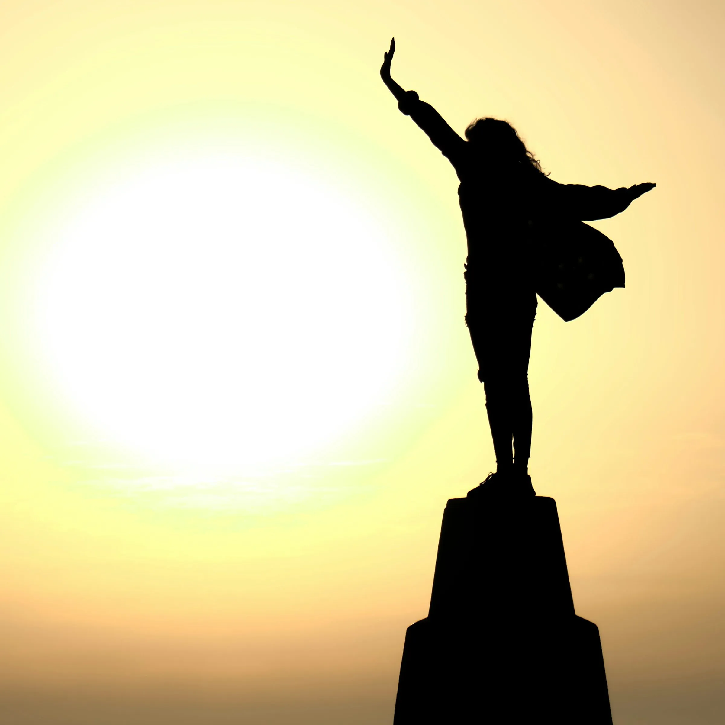 woman standing on a plinth against the sunset with arms reaching triumphantly into the air