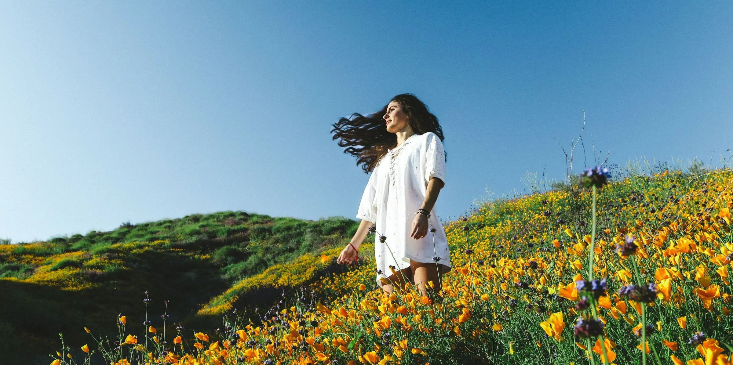 woman in white dress amongst field of flowers with blue sky